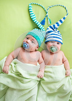 Twins infant boys babies weared in striped hats tied by heart.