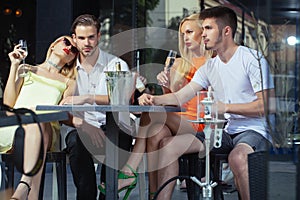 Twins women and men relax in shisha cafe outdoor