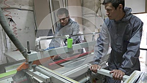 Twins workers cutting wood in carpenter workshop with table circular saw.