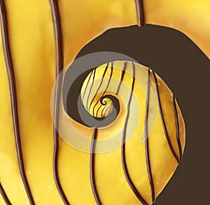 Twisted donut with banana icing and chocolate topping on brown background, spiral effect