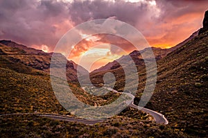 Twisty road down a mountain valley towards the sea with colorful sunset. Gran Canaria, Canary Islands