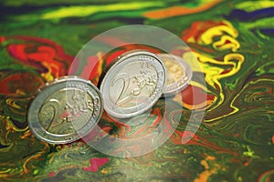Two 2 euro coins stand on edge, on a colored background.