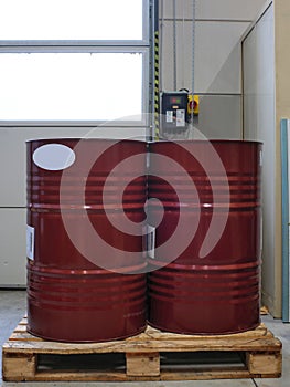 two 208 liters red metal drums on a pallet in a work area near a large door.