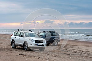 Two 4x4 jeeps on the seashore during the sunset.