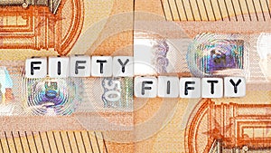 Two 50 eur banknotes and small cube beads with text FIFTYFIFTY, closeup detail from above
