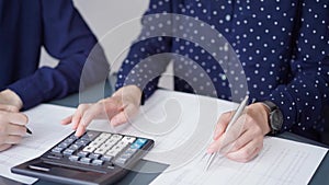 Two accountants dressed in blue are using calculator for counting taxes at grey desk in office, front side view