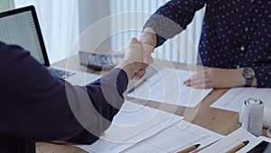 Two accountants are shaking hands after counting taxes at a wooden desk in the office. Teamwork and agreement in