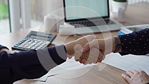 Two accountants are shaking hands after counting taxes at a wooden desk in office. Teamwork in business audit and