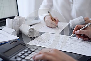 Two accountants use a calculator and laptop computer for counting taxes or revenue balance. Business, audit, and taxes