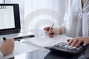 Two accountants use a calculator and laptop computer for counting taxes or revenue balance. Business, audit, and taxes