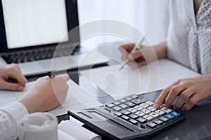 Two accountants use a calculator and laptop computer for counting taxes or revenue balance. Business, audit, and taxes