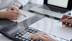 Two accountants use a calculator and laptop computer for counting taxes or revenue balance. Business, audit, and taxes