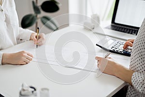 Two accountants using a calculator and laptop computer for counting taxes or revenue balance while rolls of receipts are