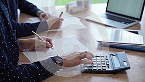 Two accountants are using a laptop computer and calculator for counting taxes at a wooden desk in office. Teamwork in