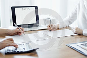 Two accountants using a laptop computer and calculator while counting taxes at wooden desk in office. Teamwork in