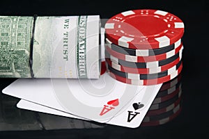 On two aces, casino chips and a roll of American dollars, on a black background with a reflection