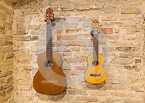 Two acoustic guitars hanging on brick wall background indoors. V