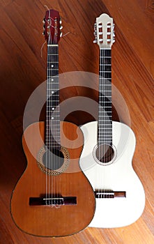 Two acoustic guitars, one light and one dark, side by side on a wooden background