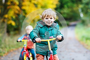 Two active brother boys running on bikes in autumn forest