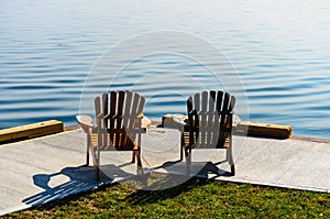 Two Adirondack chairs facing the water`s edge on a concret pier