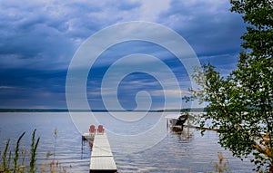 Two adirondack chairs on a pier overlooking a lake