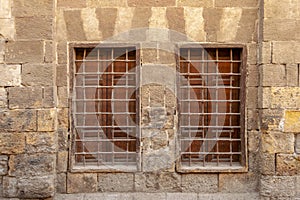 Two adjacent wooden windows with iron grid over decorated stone bricks wall, Medieval Cairo, Egypt