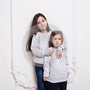 Two adorabile littles girl in sweater and jeans, posing together embraced on white background.
