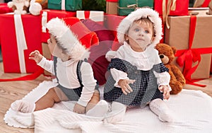 Two adorable babies sitting on floor by christmas gifts at home