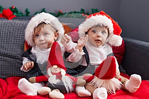 Two adorable babies sitting on sofa playing with santa claus doll at home