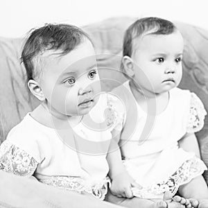 Two adorable baby twins sitting in the chair.