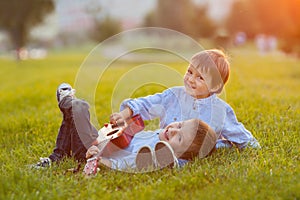 Two adorable boys, sitting on the grass, playing guitar