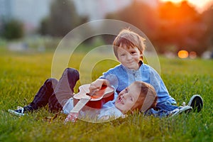 Two adorable boys, sitting on the grass, playing guitar