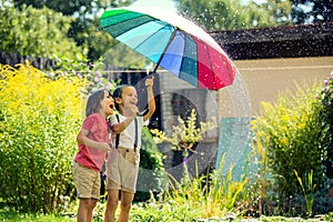 Two adorable children, boy brothers, playing with colorful umbrella under sprinkling water