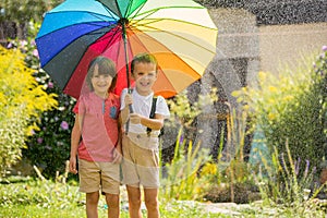 Two adorable children, boy brothers, playing with colorful umbrella under sprinkling water