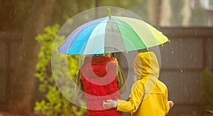 Two adorable children, boy and girl playing in park with colorful rainbow umbrella on a rainy autumn day. Child in