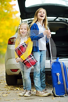 Two adorable girls with a suitcase going on vacations with their parents. Two kids looking forward for a road trip or travel. Autu