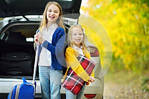 Two adorable girls with a suitcase going on vacations with their parents. Two kids looking forward for a road trip or travel. Autu