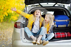Two adorable girls with a suitcase going on vacations with their parents. Two kids looking forward for a road trip or travel. Autu