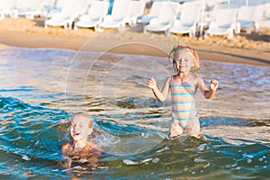 Two adorable kids playing in the sea on a beach