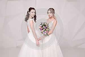 Two adorable ladies wearing in long fashionable dresses holding flowers