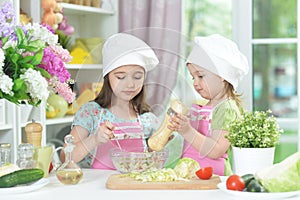 Two adorable little girls in aprons preparing delicious salad