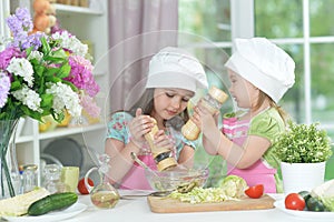 Two adorable little girls in aprons preparing delicious salad