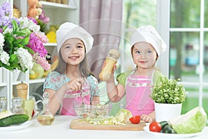 Two adorable little girls in aprons preparing delicious salad