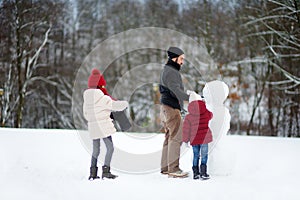 Two adorable little girls building a snowman together in beautiful winter park. Cute sisters playing in a snow.