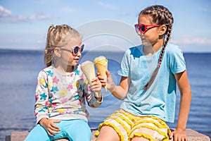 Two adorable little girls are eating ice cream on the seashore on summer vacation