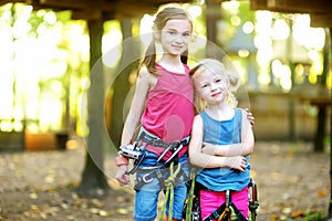 Two adorable little girls enjoying their time in climbing adventure park on warm and sunny summer day