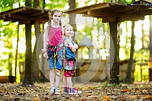 Two adorable little girls enjoying their time in climbing adventure park on warm and sunny summer day