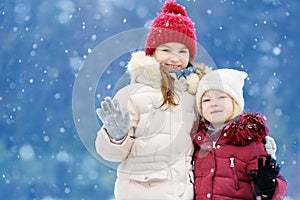 Two adorable little girls having fun together in beautiful winter park. Beautiful sisters playing in a snow.