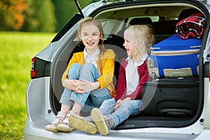 Two adorable little girls sitting in a car before going on vacations with their parents. Two kids looking forward for a road trip