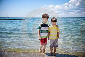 Two adorable little kid boys standing on lonely ocean beach. Child playing and looking on horizon. Vacations, summer, travel